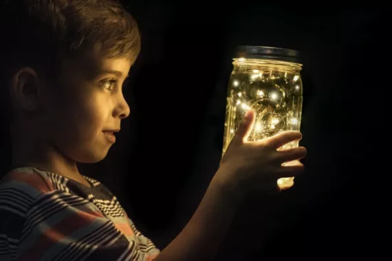 A boy looking a glow worms in a glass A boy looking a glow worms in a glass